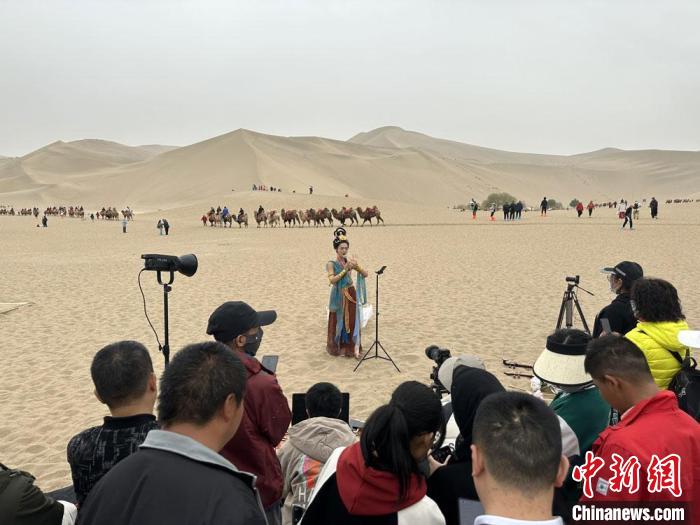 圖為2023年4月底，敦煌大漠“逐舞者”奧楠在鳴沙山月牙泉景區(qū)視頻直播，吸引游人圍觀?！●T志軍 攝